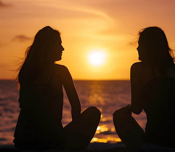 two women sitting on the beach at sunset