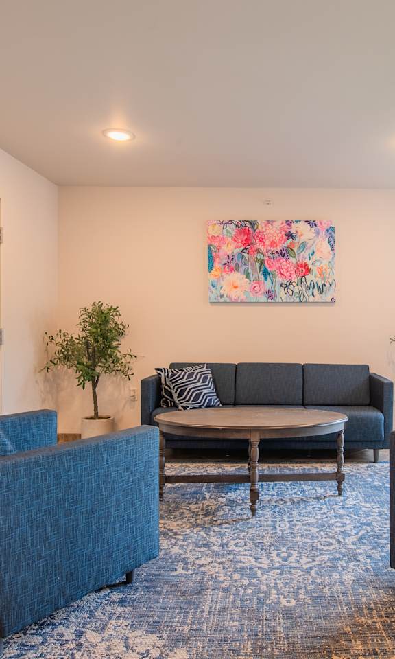 A living room with a blue rug and a painting on the wall.