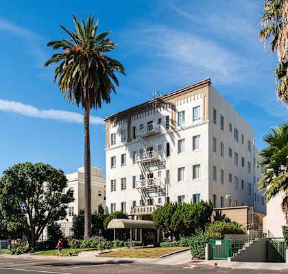 White building with a fire escape and palm trees in front of it