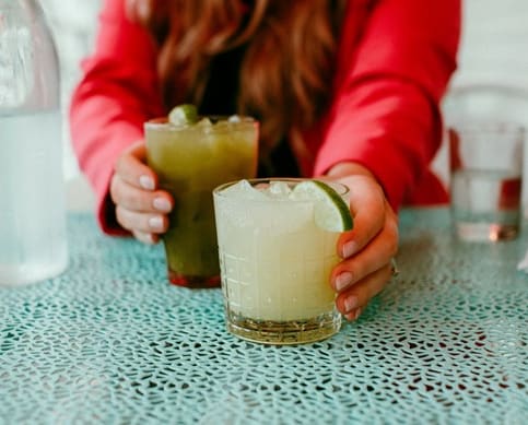 a woman sitting at a table with two drinks in front of her