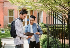 two young men standing in front of a building looking at a clipboard