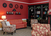 Thumbnail 11 of 17 - A living room with a red couch, two chairs, and a bookcase.