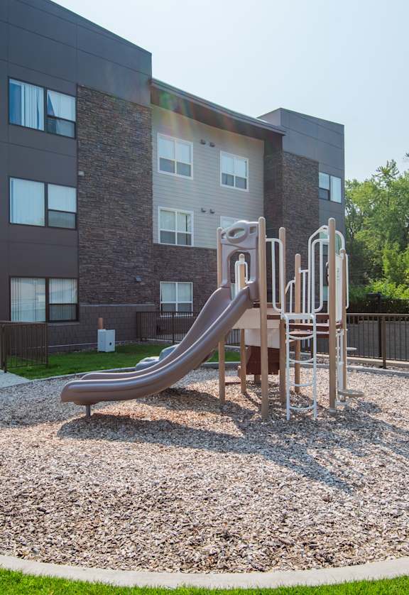 A playground with a slide and a building in the background.