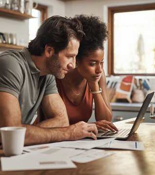 A man and a woman are looking at a laptop together in a kitchen.