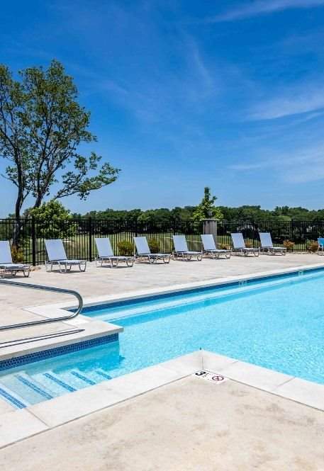 A swimming pool surrounded by lounge chairs and a fence.