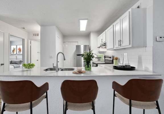 a kitchen with white cabinets and a counter with three chairs