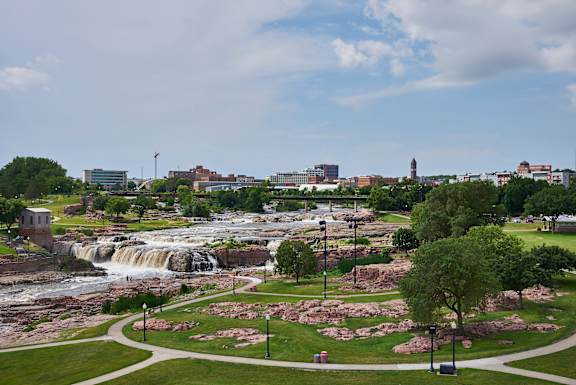 A waterfall in a park with a city skyline in the background.