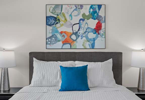 A bed with a blue pillow and a painting above it.