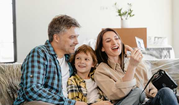 A family of three is sitting on a couch, with the woman holding a camera and taking a picture of them.