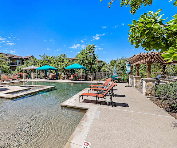a swimming pool with chairs and umbrellas in front of a house at Lakeline East Apartments, Texas, 78613