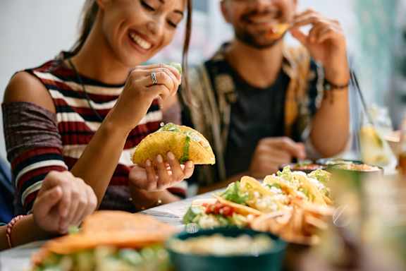 A woman and a man are enjoying tacos at a table.