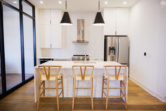 Kitchen with white cabinets and a white island with three wooden stools