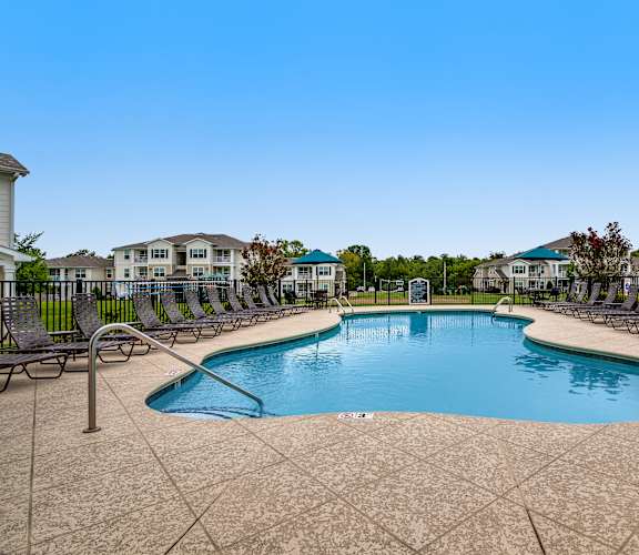 A large swimming pool surrounded by lounge chairs and a fence.
