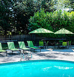 a swimming pool with green chairs and umbrellas next to a resort style pool