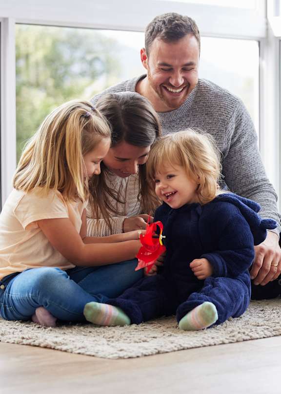 A family of three is sitting on the floor in a bright room.