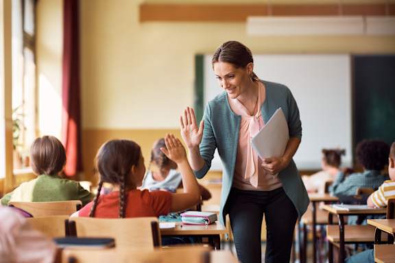 A woman in a pink scarf is teaching a class of children in a classroom.