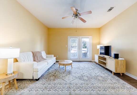 A living room with a white couch, a wooden coffee table, a television, and a ceiling fan.
