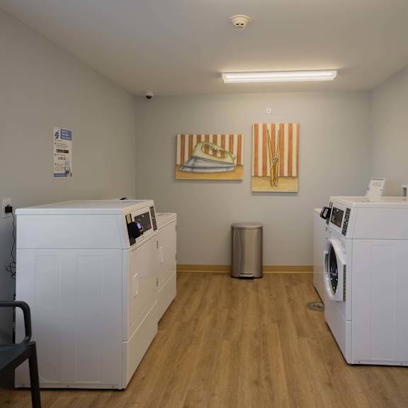 A laundry room with a washer and dryer on each side and a chair in the middle.