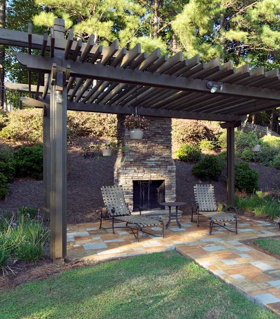 A patio with a fireplace and chairs under a wooden pergola at Austin Chase Apartments, Georgia