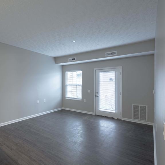 A room with a door, two windows, and a light switch on the wall.