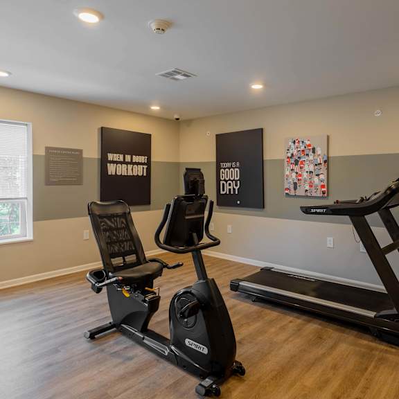 A room with a treadmill, a stationary bike, and a sign that says "Good Day" on the wall.