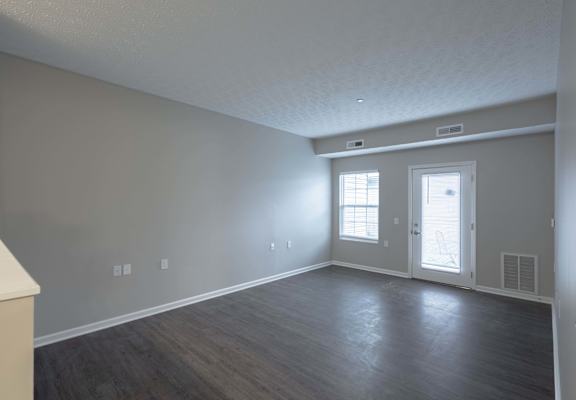 A room with a door, two windows, and a light switch on the wall.