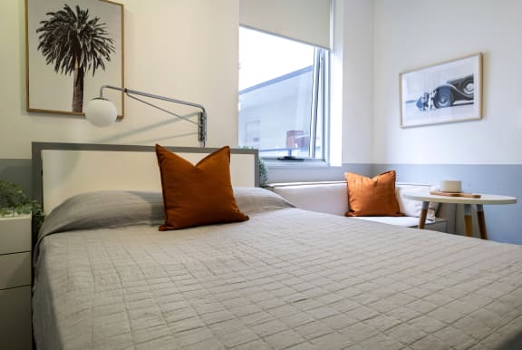 a bed with two orange pillows in a room with a window