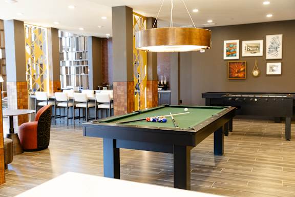 A billiard table is in the middle of a room with a bar and chairs. at District on the Etowah Apartments, Canton Georgia