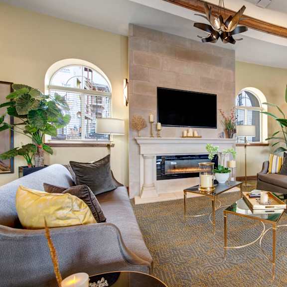The clubhouse at La Bella Vita, with two plush couches and throw pillows, coffee tables, house plants, artwork, candles, and a TV on the wall. 