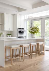 A modern kitchen with a white island and wooden stools.
