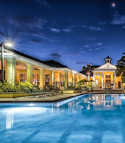 a large swimming pool with chaise lounges and palm trees in front of a large