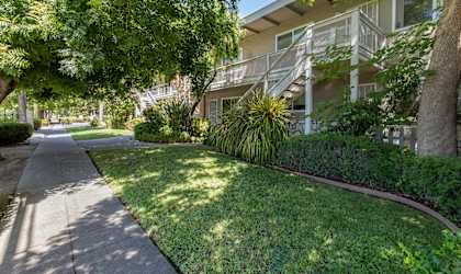 a sidewalk in front of an apartment building with grass and trees