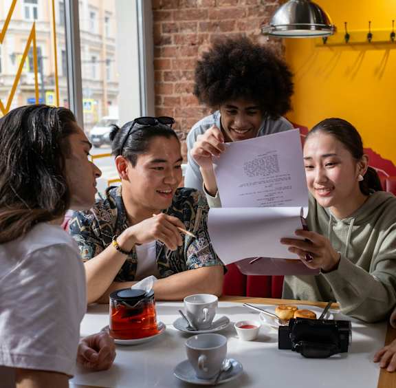 a group of people sitting around a table in a restaurant reading a piece of paper