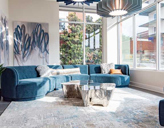 Modern living room with a blue sectional sofa, abstract wall art, large windows, and metallic coffee tables at NOVI
