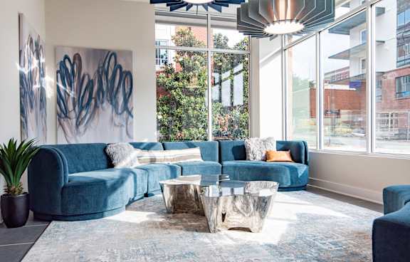 Modern living room with a blue sectional sofa, abstract wall art, large windows, and metallic coffee tables at NOVI