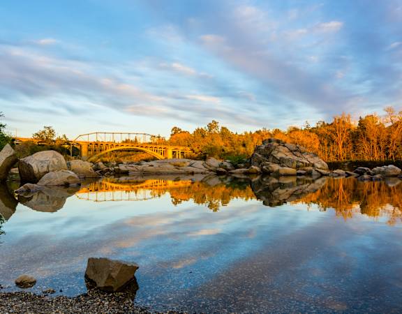 A serene landscape with a bridge reflected in the water.