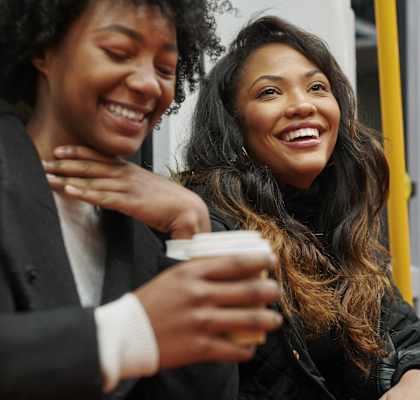 Two people are sitting on a bus, one is holding a cup.