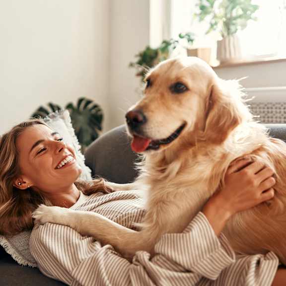 A woman is hugging a golden retriever on a grey couch.