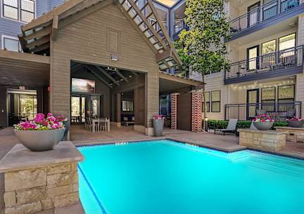 A swimming pool surrounded by lounge chairs and umbrellas in front of apartment buildings.