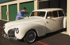 A man is opening the trunk of a white vintage car.