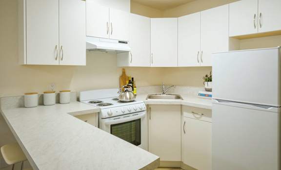 A white kitchen with a stove, sink, and refrigerator.