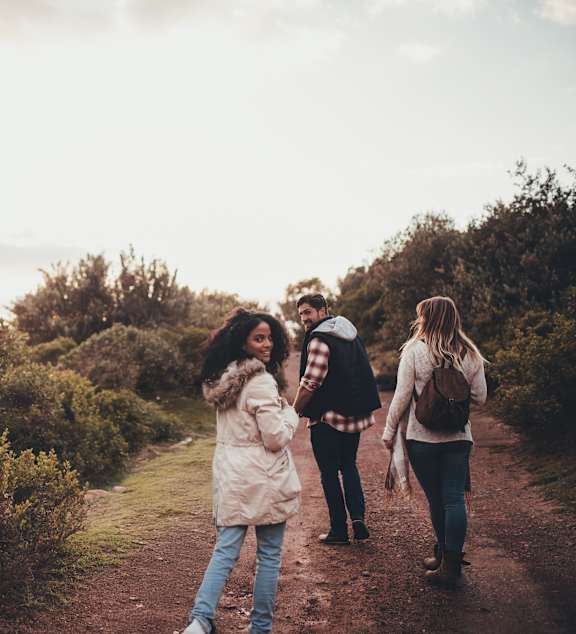 Four people walking on a dirt path through a natural landscape.