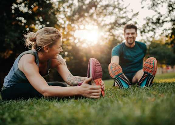 A man and a woman are stretching their legs in the grass.
