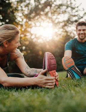 a man and woman sitting on the grass touching their shoes