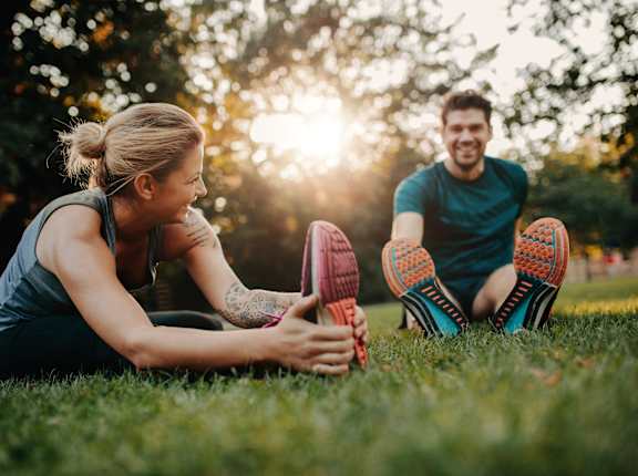 a man and woman sitting on the grass touching their shoes