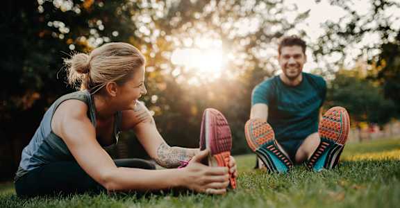 a man and woman sitting on the grass touching their shoes