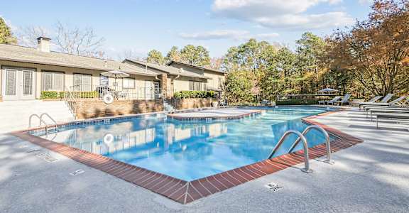 A swimming pool surrounded by a brick border and lounge chairs.