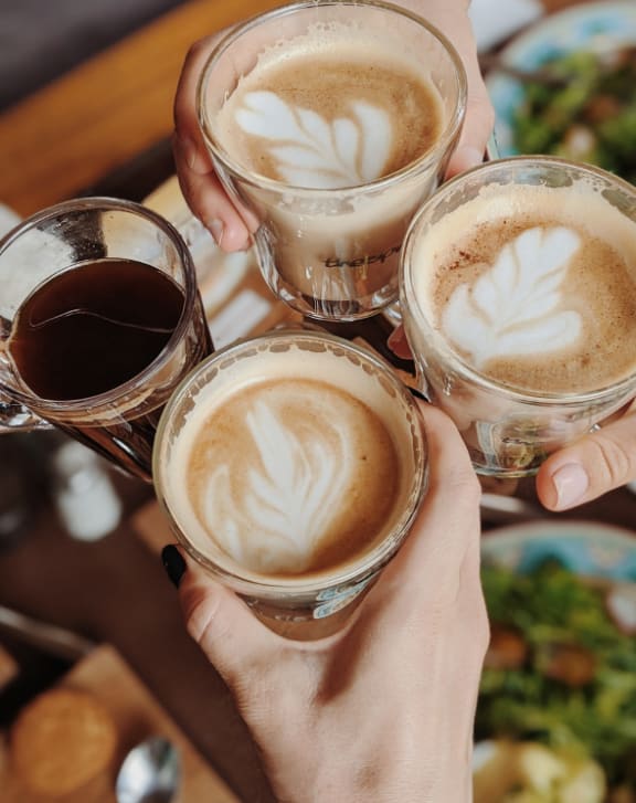 a group of people holding up four glasses of coffee