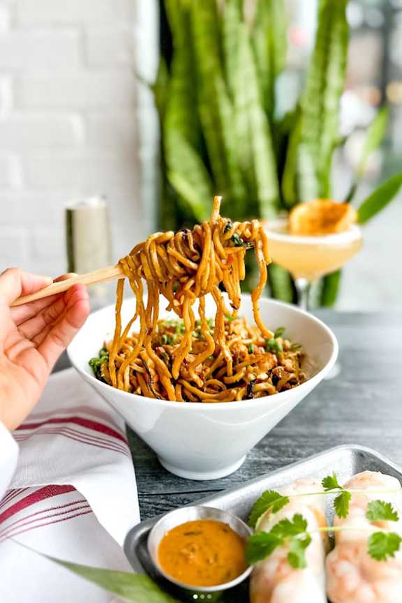 A person is holding chopsticks with some noodles in them.