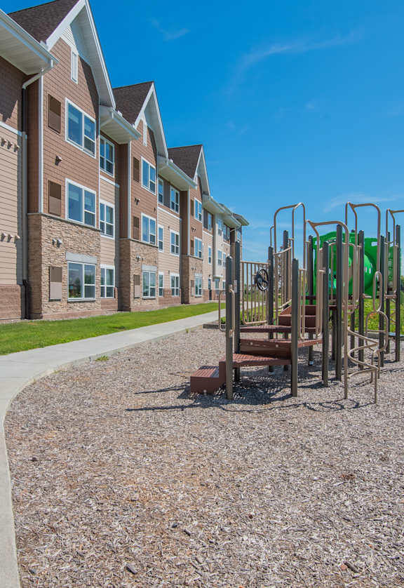 A playground with a swing set is located in front of a building with a paved walkway.